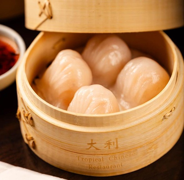 A bamboo steamer with four plump shrimp dumplings, served alongside a small bowl of dipping sauce.