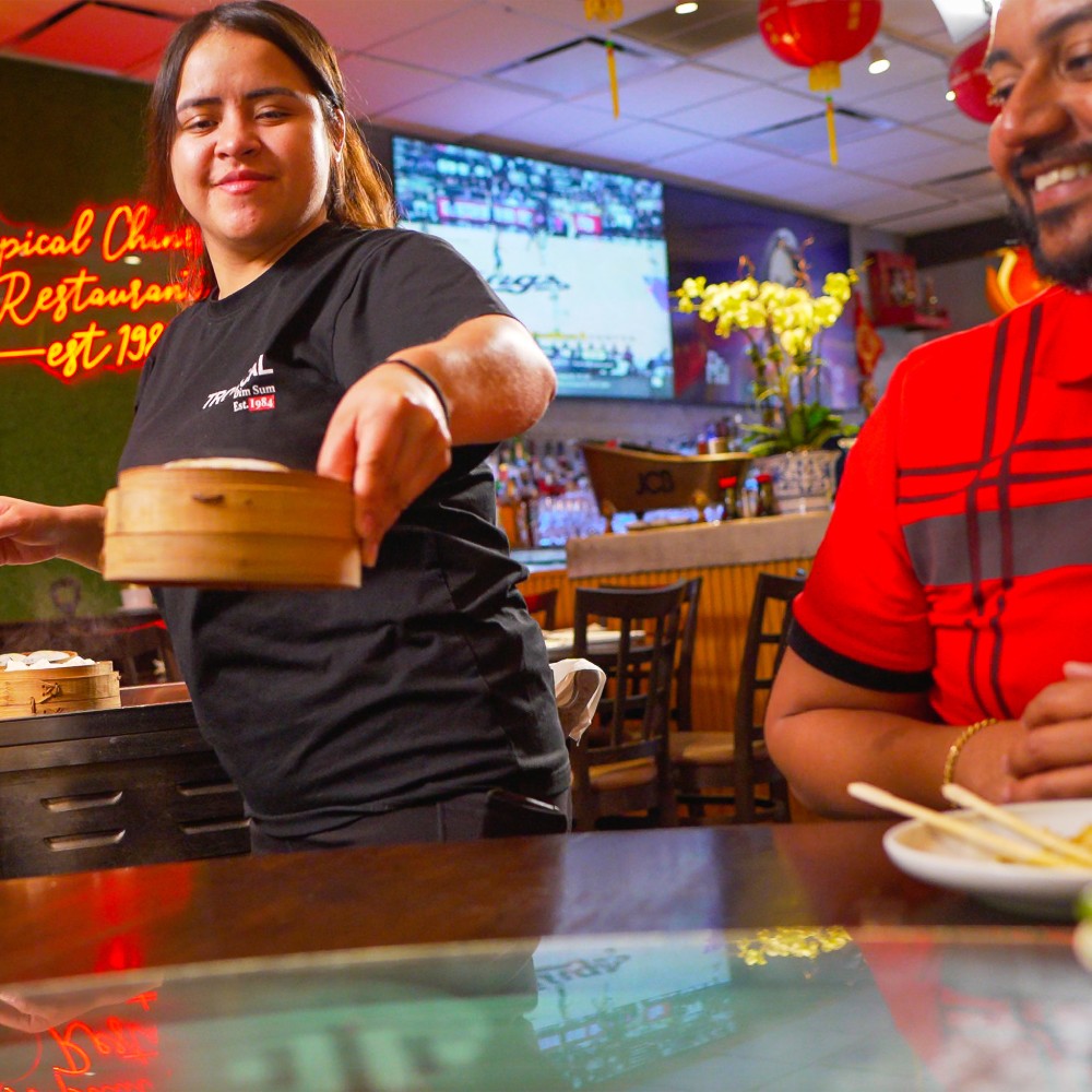 A server delivers food in a warmly lit restaurant with red lanterns, and flowers