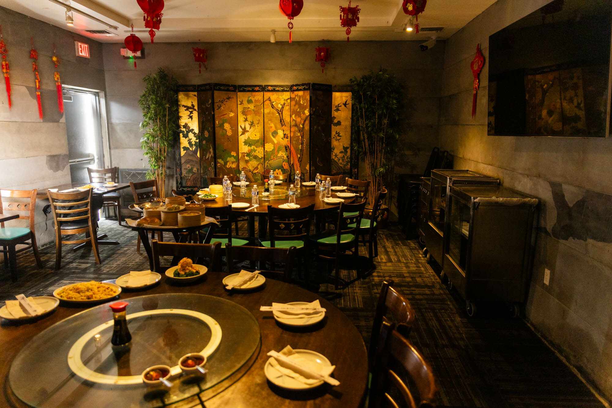 Warmly lit Chinese dining room with a round table set for a meal, surrounded by red lanterns, floral decor, and traditional accents.
