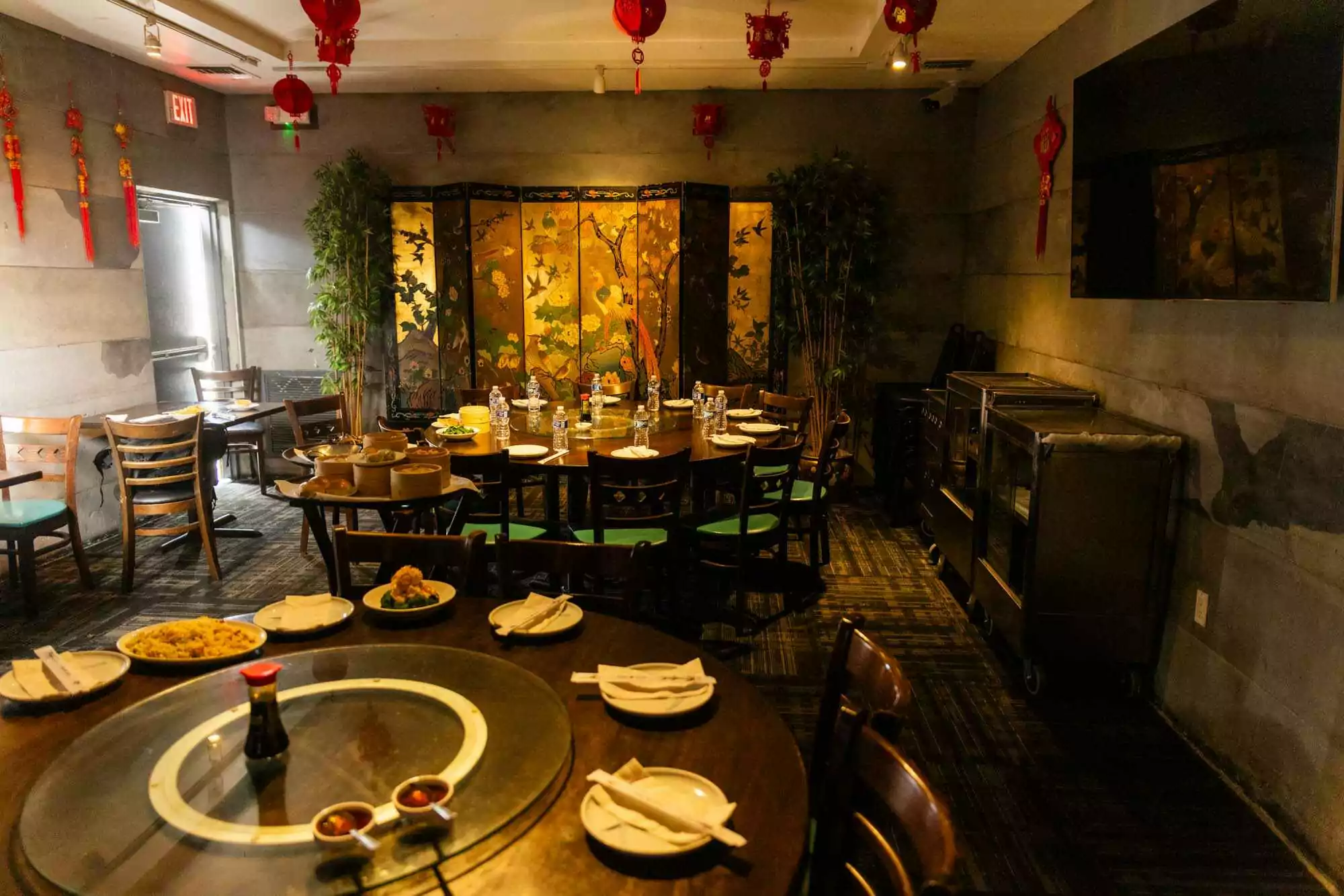 Warmly lit Chinese dining room with a round table set for a meal, surrounded by red lanterns, floral decor, and traditional accents.